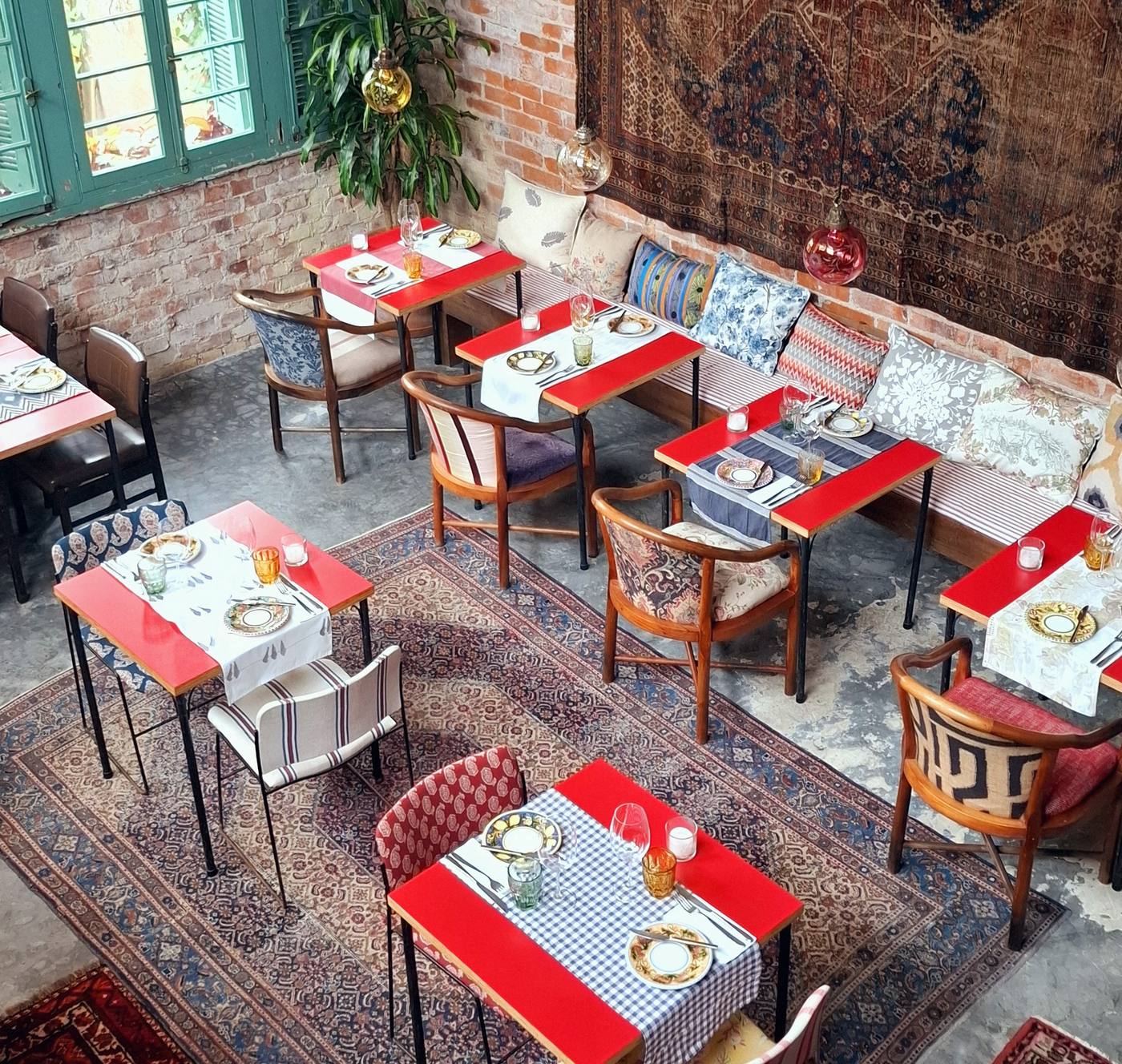 Vista de cima do salão do Aora Cucina, com mesas coloridas, tapetes persas e almofadas estampadas