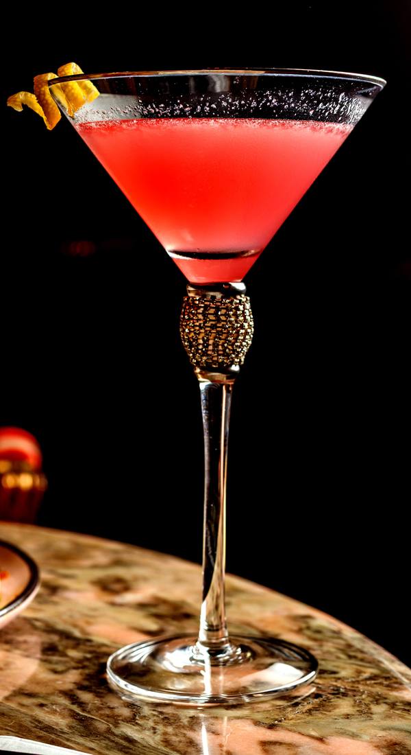 Taça de cosmopolitan rosa com casca de laranja sobre mesa de mármore