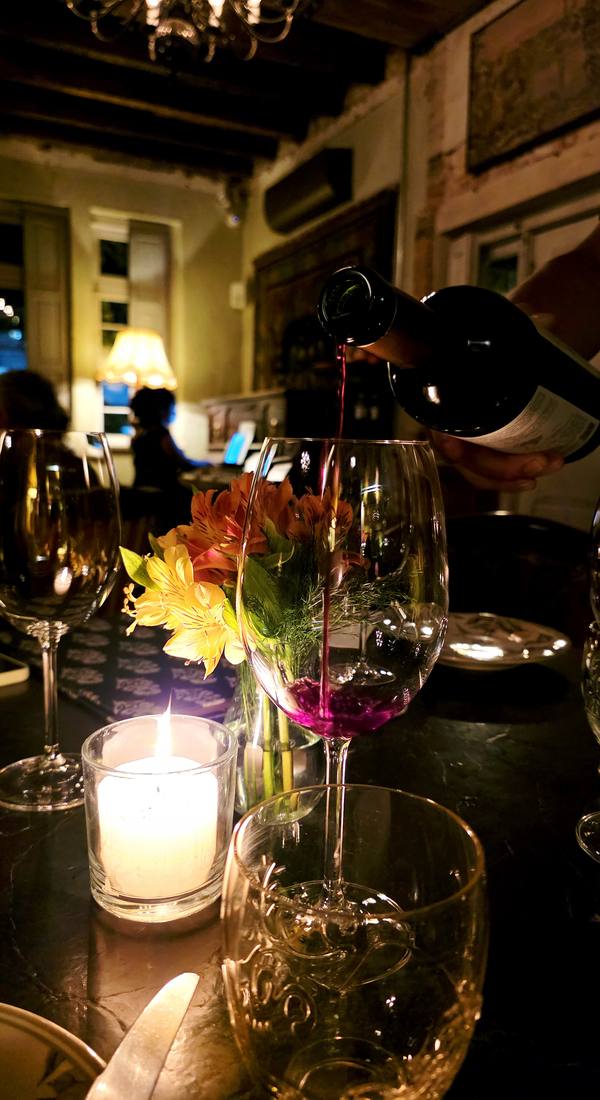 Taça de vinho tinto sendo servida à luz de velas, com flores sobre a mesa