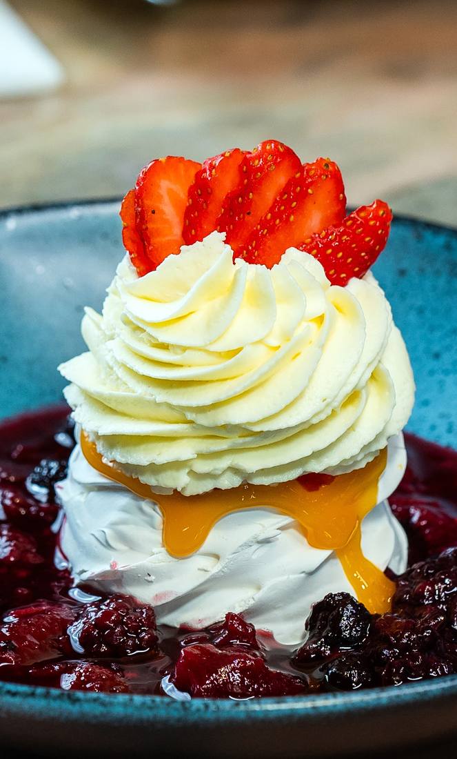 Pavlova com chantilly, morangos frescos, molho de frutas vermelhas e calda de doce de ovos
