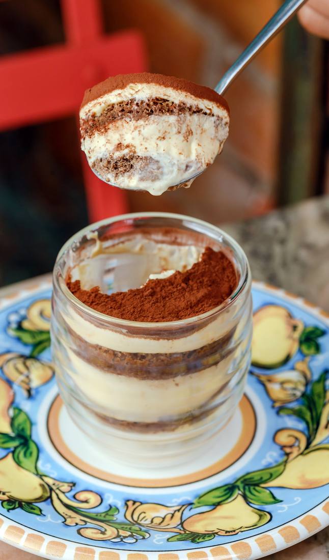 Tiramisù em camadas, servido em copo, com colher erguendo uma porção
